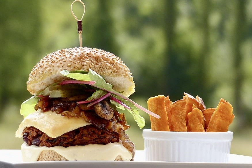 Artisanal vegan burger featuring a plant-based patty with melted dairy-free cheese, caramelized onions, and fresh greens on a sesame seed bun, paired with golden sweet potato wedges. A wholesome plant-forward take on comfort food for longevity and wellness.