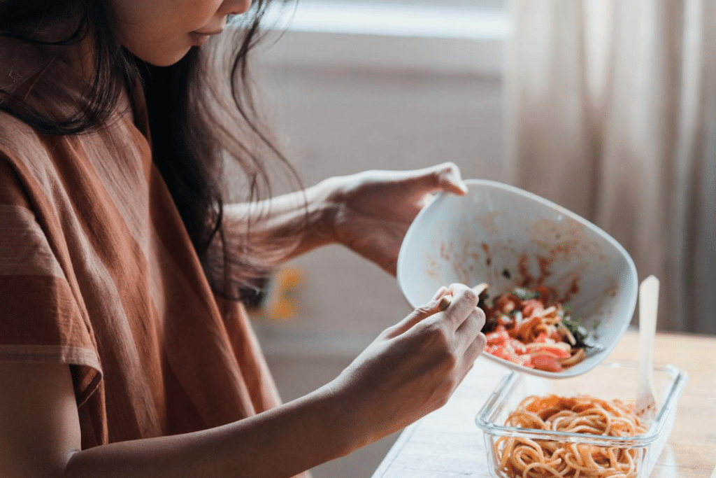 Woman preparing healthy meal from glass containers, portioning food in natural lighting near window