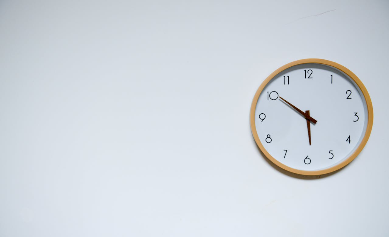 Analog wall clock with wooden frame against white wall, illustrating optimal daily workout timing for enhanced sleep quality and longevity. The minimalist clock emphasizes the importance of exercise scheduling for better sleep patterns and a longer life