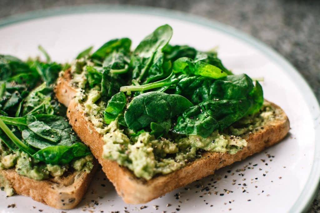 Fresh avocado toast topped with vibrant spinach leaves and seeds, demonstrating simple mindful plant-based meal preparation