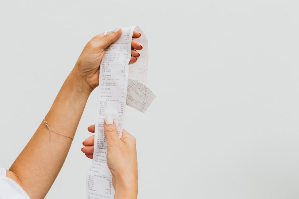 Hands holding a long receipt, symbolizing cost-conscious shopping and savings.