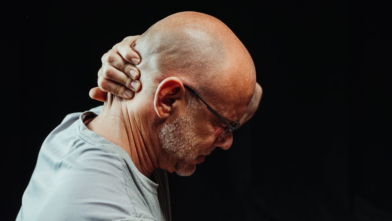 Bald man massaging neck in pain, demonstrating physical signs of inflammation and chronic discomfort