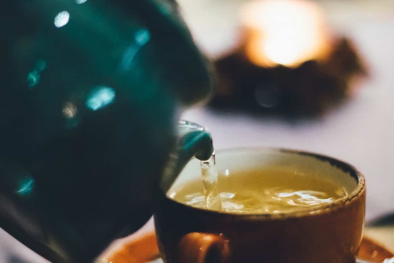 Pouring therapeutic green tea from a teal teapot, capturing the moment this antioxidant-rich longevity beverage streams into an earthen cup. Close-up macro shot highlighting the catechins and polyphenols in green tea, renowned for their anti-inflammatory properties and cellular aging benefits. A daily ritual in traditional wellness practices for reducing inflammation and supporting healthy aging