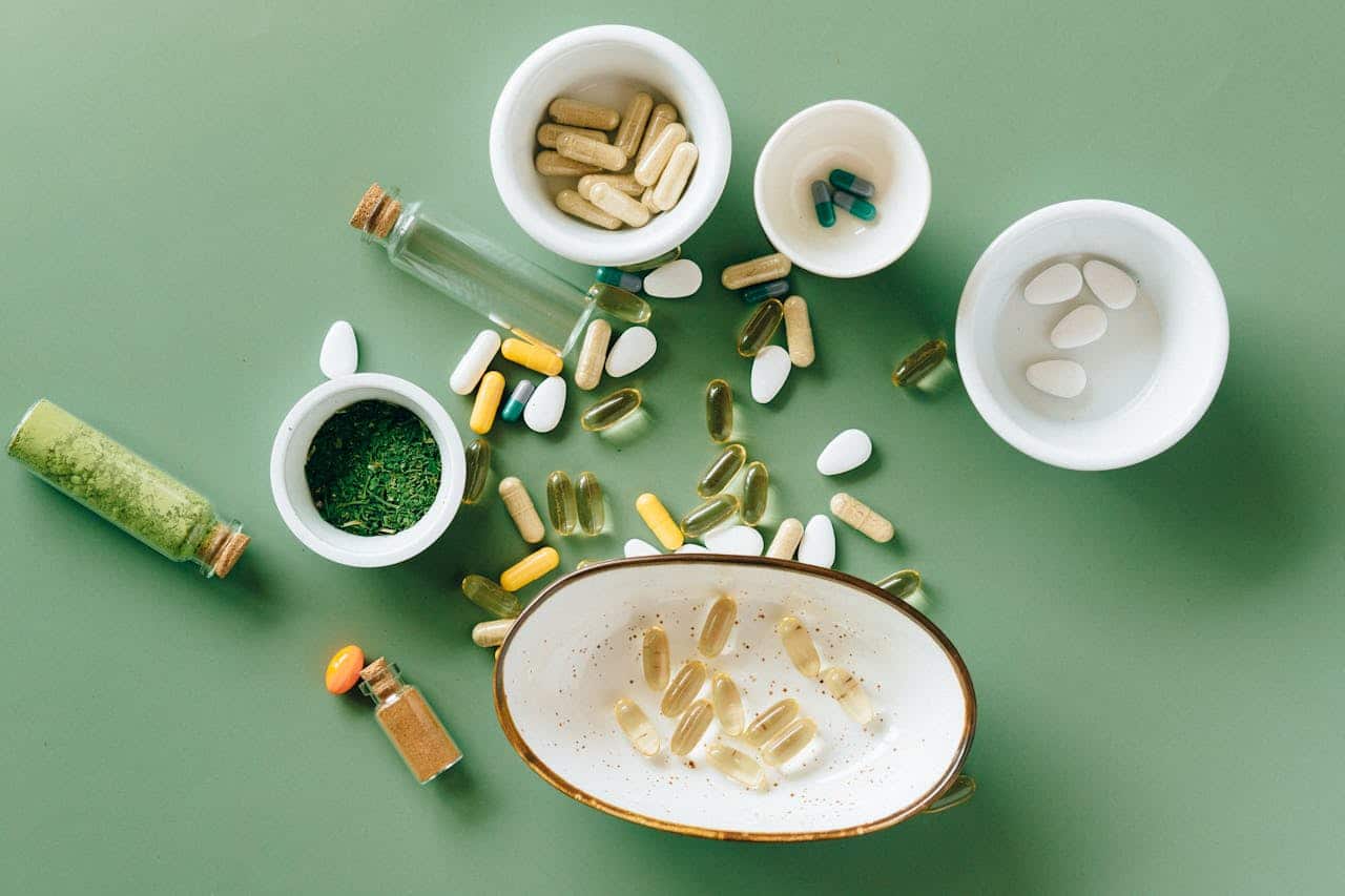 Natural supplements and anti-inflammatory vitamins including probiotics, omega-3 capsules, herbal powder, and mineral tablets arranged in white ceramic bowls on a green background. Essential longevity supplements and holistic wellness products displayed in a minimalist, clinical aesthetic with glass vials containing natural extracts