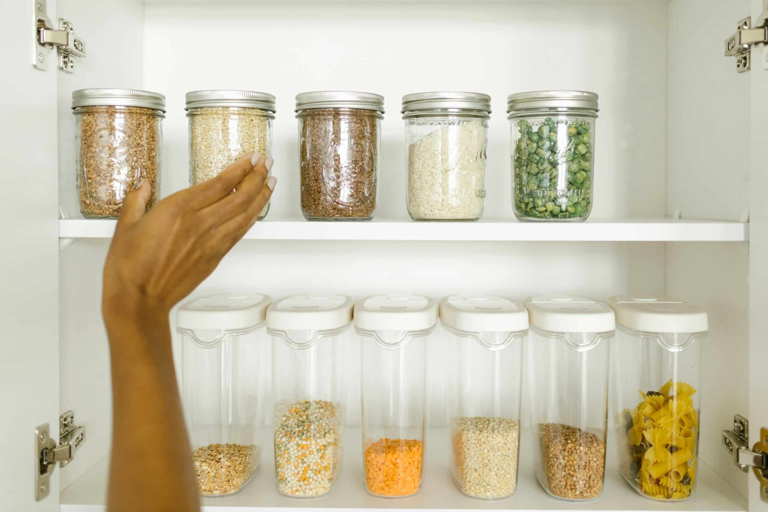 Organized pantry with mason jars and containers of whole grains, legumes, and plant-based staples showing mindful food storage and preparation