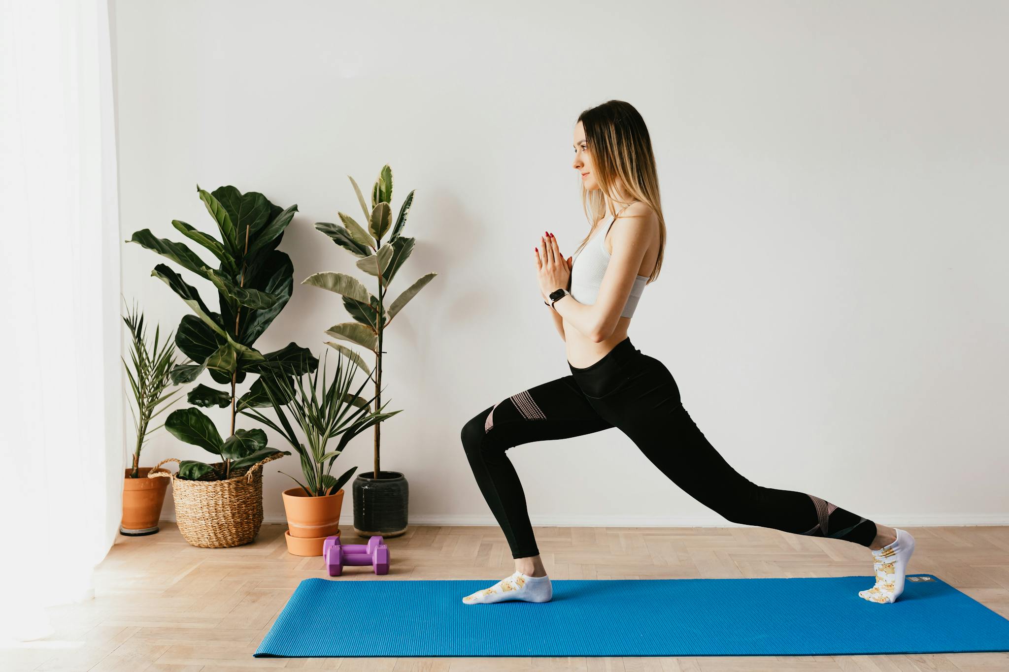 Woman in comfortable athletic wear practices yoga on a mat, demonstrating mindful movement and balanced posture. In a sunlit, minimalist setting, her calm demeanor and intentional form illustrate the connection between gentle exercise, reduced inflammation, and healthy aging practices.