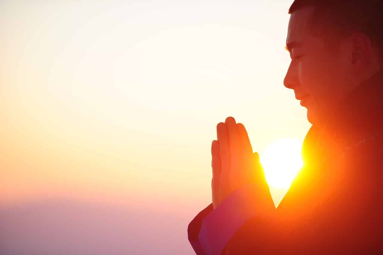 Loving-kindness meditation practice at sunset: person with hands in prayer position practicing mindful gratitude and inner peace meditation techniques during golden hour