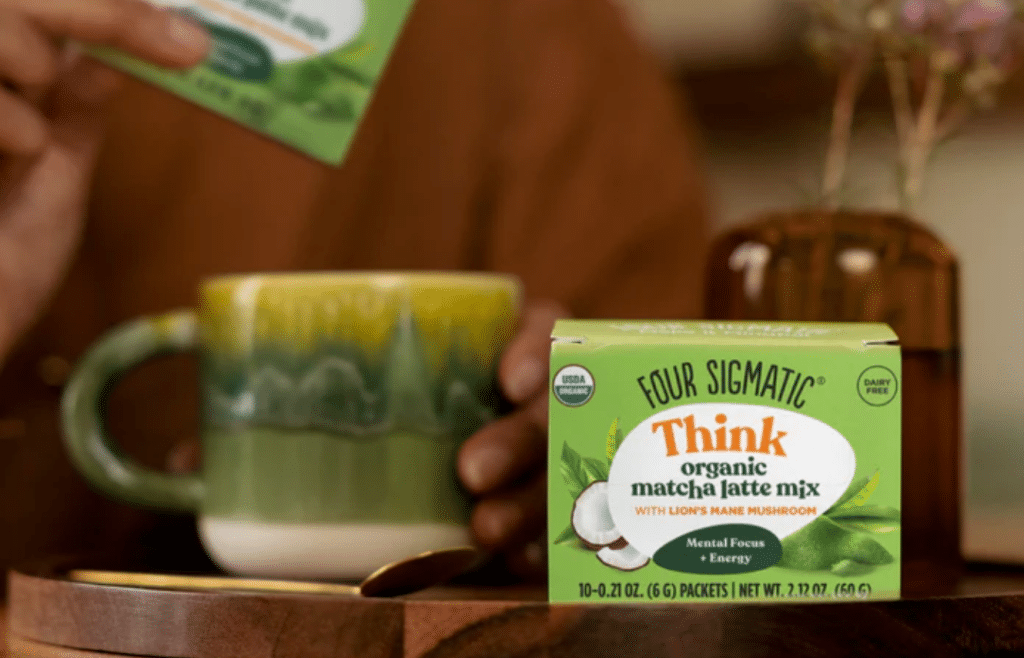 Four Sigmatic Think organic matcha latte mix with Lion's Mane mushroom in a green box, placed next to a ceramic green mug on a wooden surface, promising mental focus and energy benefits.