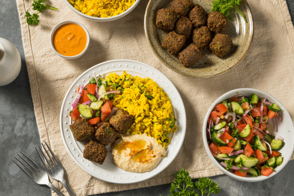 A Mediterranean plant-based meal with falafel, golden turmeric rice, hummus, and a fresh cucumber-tomato salad, served on a rustic table setting.