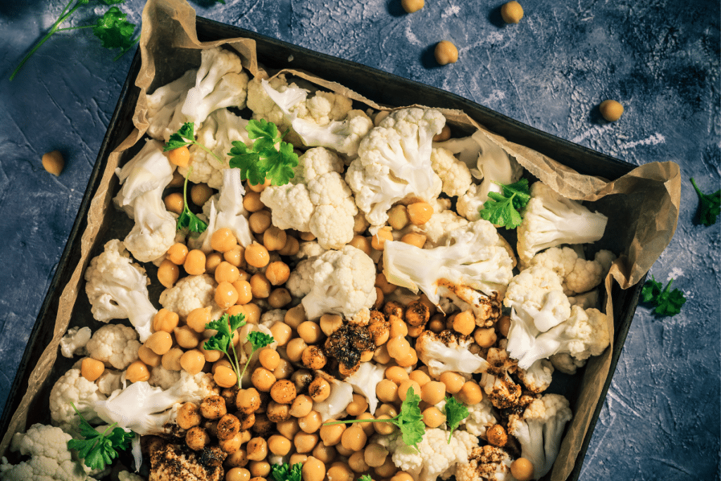 A sheet pan filled with cauliflower, chickpeas, and roasted spiced chickpeas, garnished with fresh parsley.