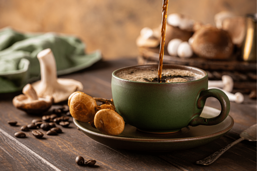Mushroom coffee being poured into a rustic green ceramic mug on a wooden table, surrounded by coffee beans and various medicinal mushrooms.  