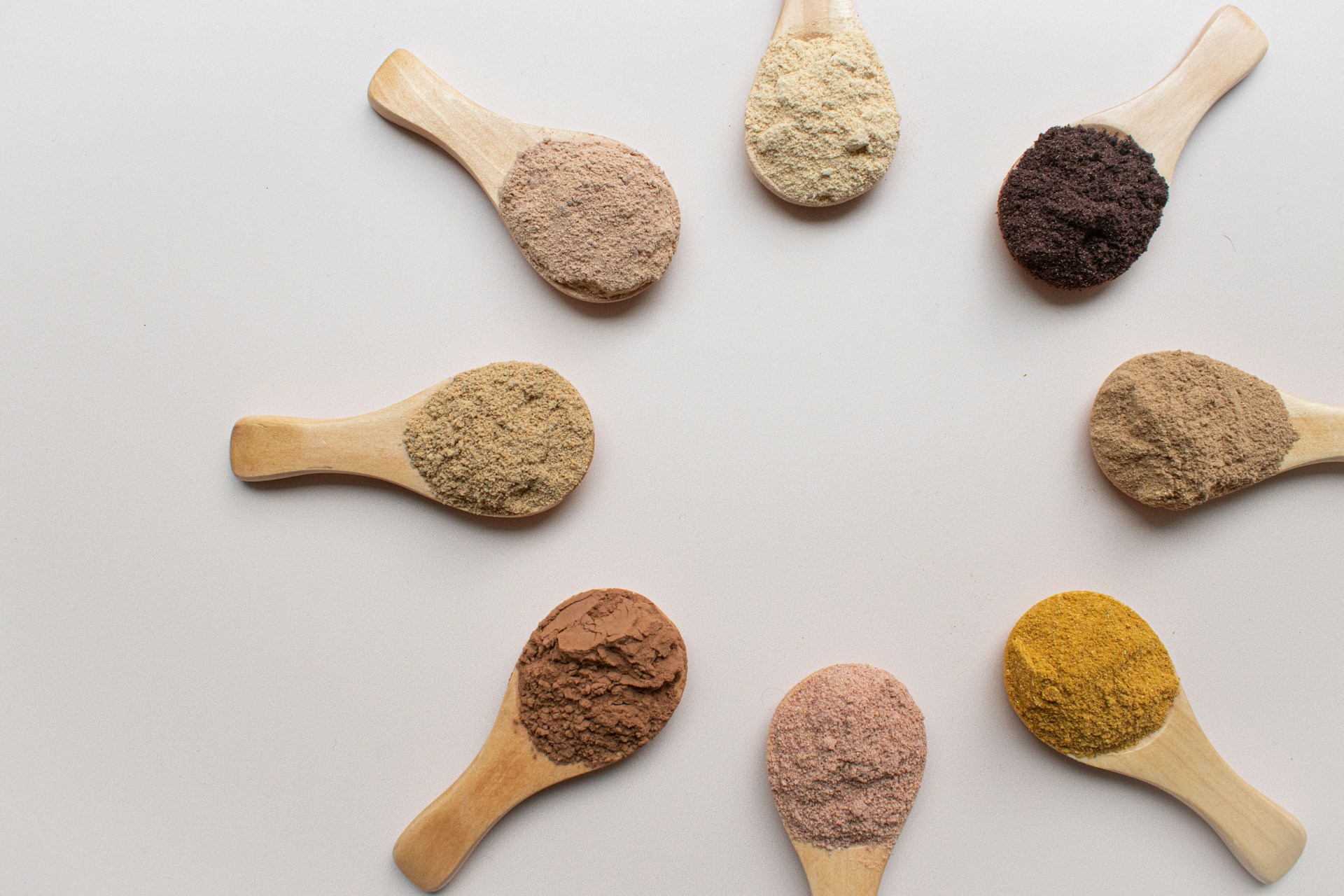 Various adaptogen powders are displayed in a circular arrangement on wooden spoons, showcasing natural herbs like ashwagandha and lion's mane, which are used for stress relief, focus, and energy.