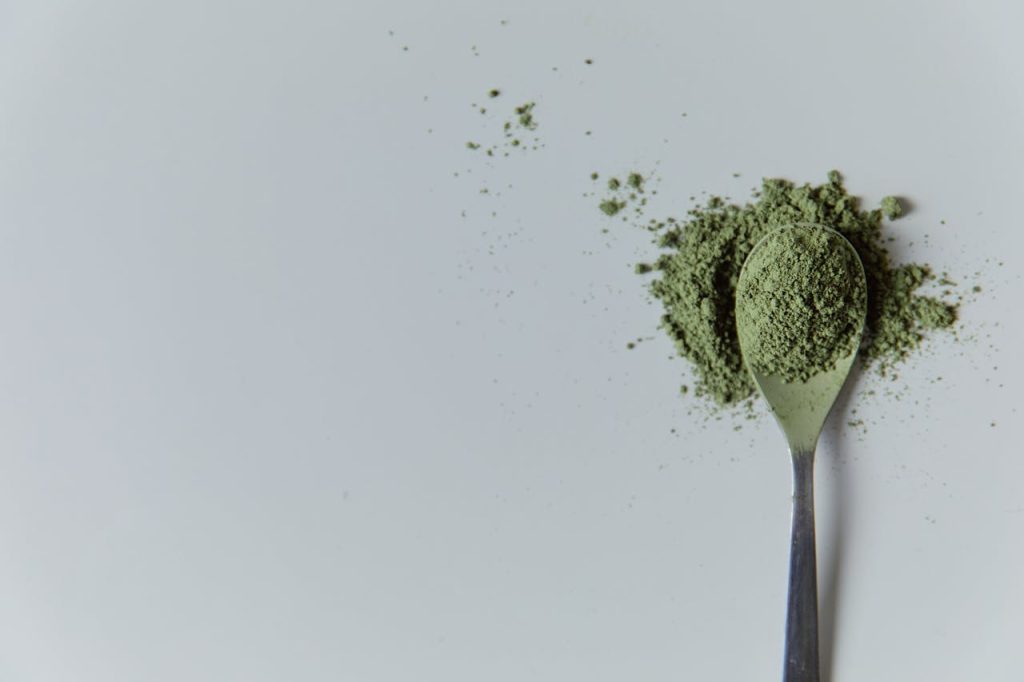 Finely ground bright green matcha powder on a silver spoon against a white background, showcasing its vibrant color and fine texture