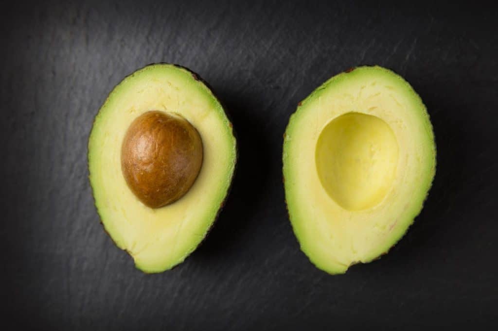 Fresh halved avocado displaying its creamy yellow-green flesh and brown pit against a dark background, showing perfect ripeness