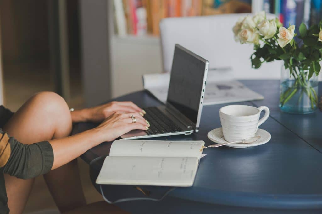 The person working on a laptop with mushroom coffee and a notebook showing focused mental clarity and productivity