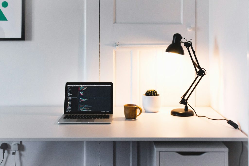 Clean workspace setup with a laptop, mushroom coffee cup, and desk lamp showing a focused productivity environment