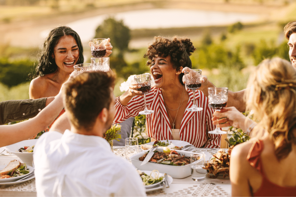 A joyful group of friends sharing a meal and wine outdoors, reflecting the Blue Zone habit of strong social connections and moderate alcohol consumption for longevity.