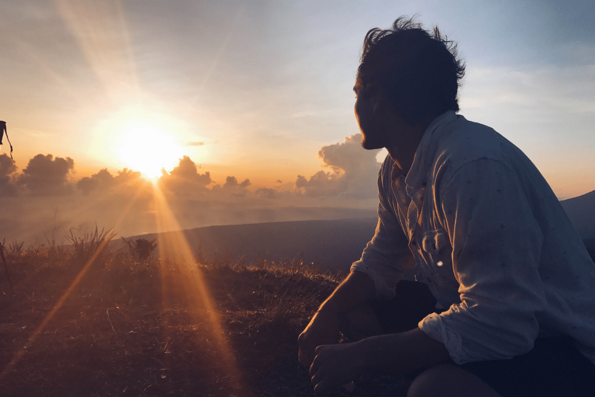 Person enjoying incredible sunlight benefits during sunset, sitting on hillside experiencing natural mood enhancement and vitamin D production