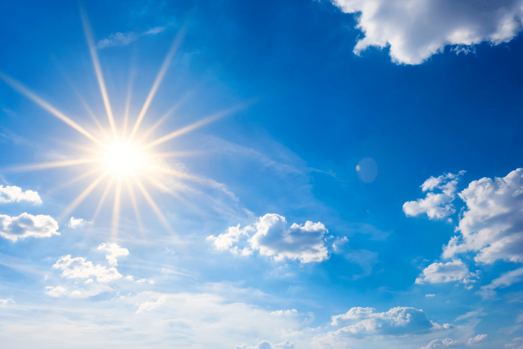 A bright sun shining in a clear blue sky with scattered clouds, symbolizing the natural energy and health benefits of sunlight.